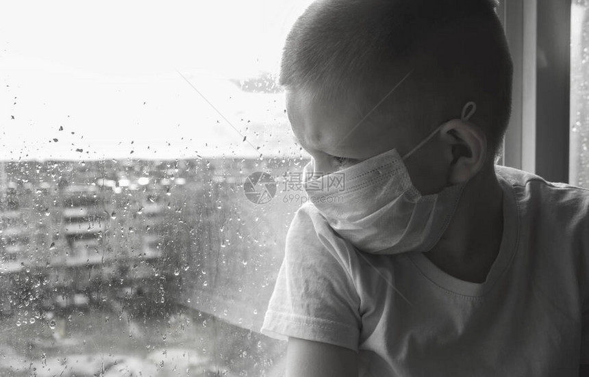 冠状自我隔离和检疫的概念一个戴着一次医用口罩的男孩带着雨滴看着窗图片