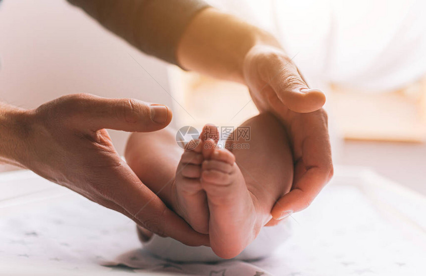 新生婴儿的特写脚年轻的父亲抱着婴儿的脚在他的手中小婴儿躺在孩子们的桌子上靠近窗户的婴儿换尿布图片