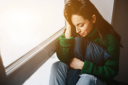 不快乐的年轻女人在窗户附近很伤心黑发女郎在哭悲伤冷漠背景图片