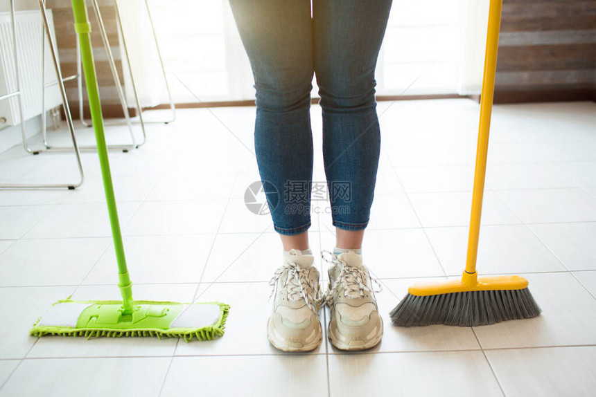 隔离期间厨房里的年轻女子用绿色拖把和黄色扫帚站在地板上白天的清洁时间一个人在厨图片