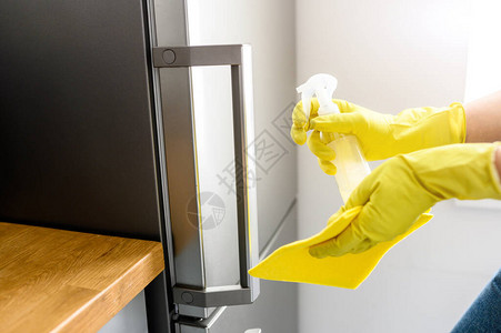 一个戴着防护橡胶手套的女人的手正在清洁和消毒冰箱的把手图片