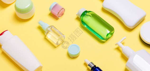 黄色背景上不同大小的化妆品罐和瓶子组成图片