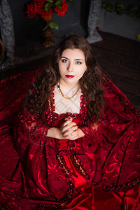 一个美丽的女孩穿着洛科时代的一身壮丽红衣坐在壁炉和鲜花背景图片