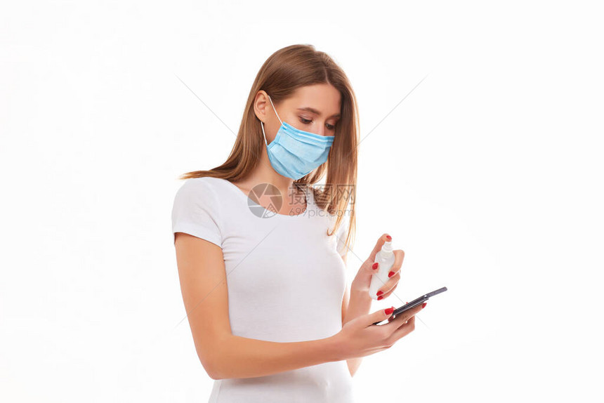身戴医疗面具的年轻妇女用凝胶防疫喷雾剂洗了手机图片