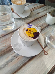 的卡布奇诺咖啡装饰着一张木桌上的鲜花和一杯水阳光下图片