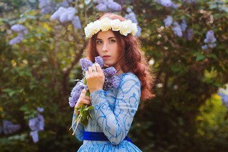 穿着蓝色华丽礼服的迷人女在花朵开花的背景下在公图片