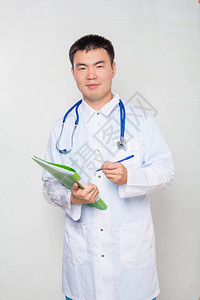 一位身着白大衣脖子上有听诊器的亚洲年轻医生手里握着绿色文件夹并作笔记图片