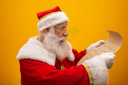 快乐的圣诞老人拿着黄色背景的老式纸圣诞快乐和前夜的概念复制空间阅读困难背景图片