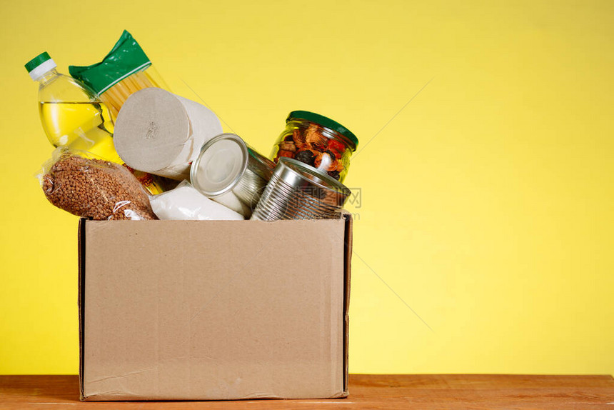 食物捐赠概念与食物的捐赠箱在黄色背景的捐赠在冠状大流行的背景下向老图片