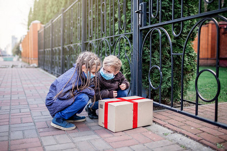 一个戴着医用口罩和手套的孩子看着在现代住宅门口附近交付了一个纸板箱图片