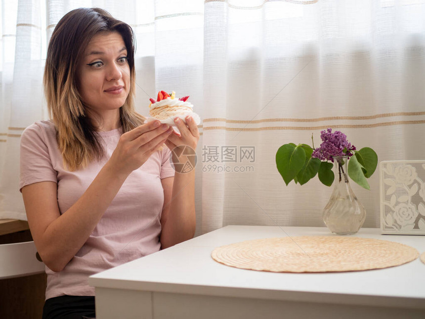 一个穿着粉红色T恤的女人坐在白桌边想对垃圾食品说不带水果的糖蛋糕图片