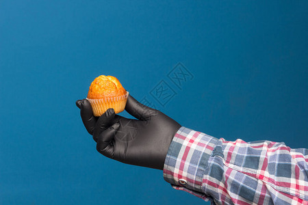 手中的工业纸杯蛋糕用蓝色背景的黑色手套消毒和保图片