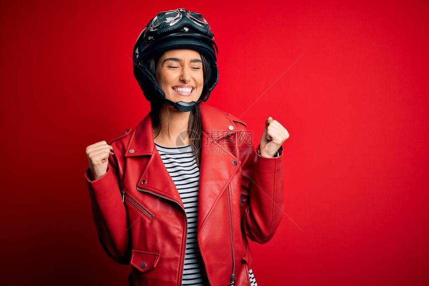年轻漂亮的黑发摩托车手戴着摩托车头盔和红色夹克图片