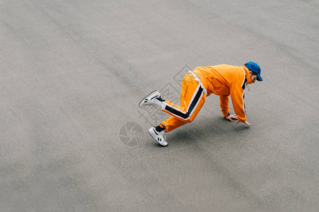 穿着橙色衣服的年轻人在沥青上展示街头嘻哈舞蹈图片