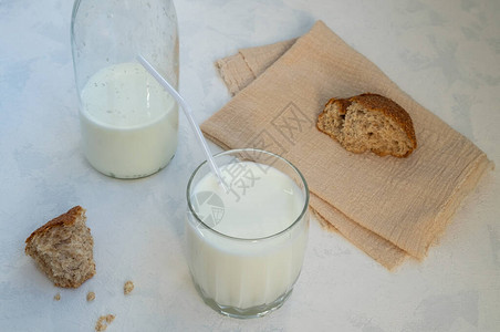 特写玻璃杯牛奶半空奶瓶和碎全麦面包图片