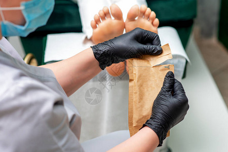 修指甲大师在修脚手术前用戴着黑色手套和面具的修指甲工具打开工图片