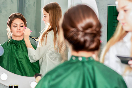 镜子化妆师在美容院为年轻女做专业化妆图片