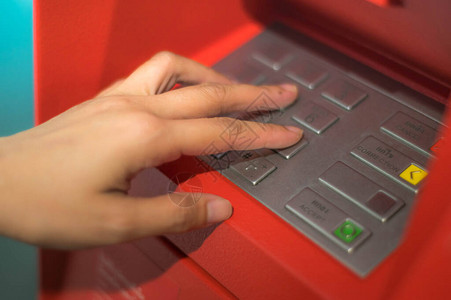 女人双手按下红色柜子里的ATM钥匙手指按数字键盘上的pin码红色自动取款机ATM背景图片