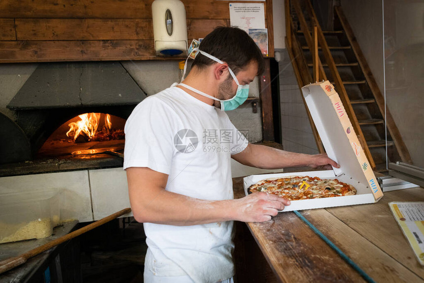 男人带着面具在一家比萨饼餐厅的驱动器里工作图片