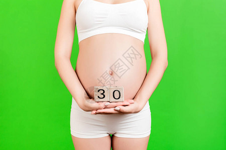 关闭穿着白色内衣的孕妇拿着带有怀孕周数的立方体在绿色背景下怀孕三十图片
