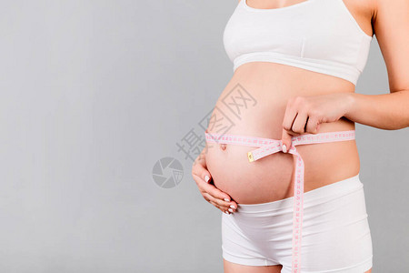 灰色背景下穿着白色内衣的孕妇腹部卷尺的特写测量生长的腹图片