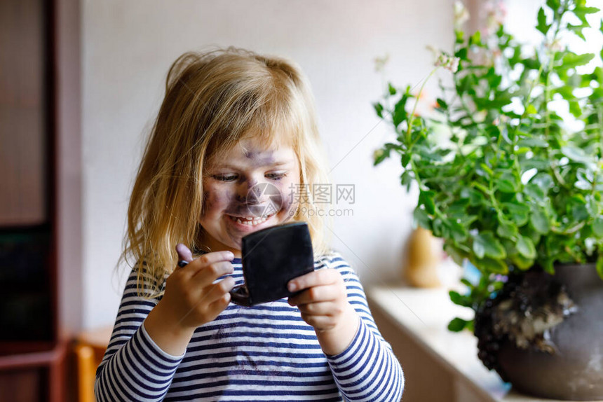 有趣的蹒跚学步的小女孩用妈化妆和画眼影的脸图片