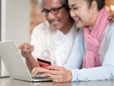 特写手持信用卡的亚洲老年夫妇在家中处理财务时开心地使用笔记本电脑科技图片
