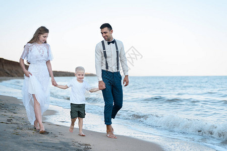 美丽的年轻夫妇和小男孩在海滩散步父母亲图片