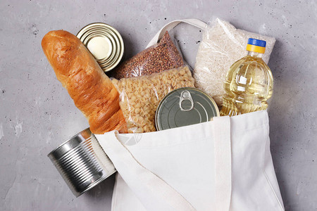 食品配送灰色混凝土背景上带有食品供应的纺织购物袋大米荞麦面食面包罐头食品植物油捐赠图片