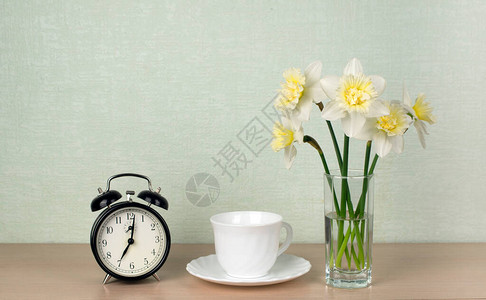 一束水仙花一杯茶或咖啡一个金绿石背景的机械闹钟早餐文本场所图片