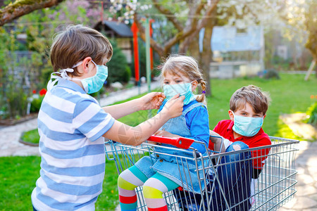 三个孩子蹒跚学步的小女孩和两个戴着医用口罩的男孩图片