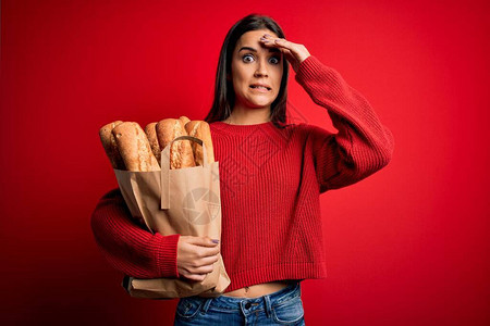 年轻美丽的黑发女人拿着纸袋和面包在红色背景上图片