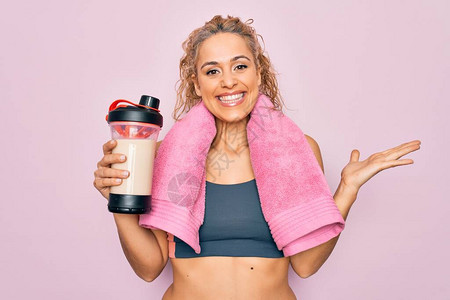 漂亮的金发运动女穿着毛巾拿着振动筛和蛋白质饮料做运动图片