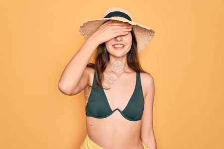穿着泳衣比基尼和夏日太阳帽的年轻美女在黄色背景下笑图片