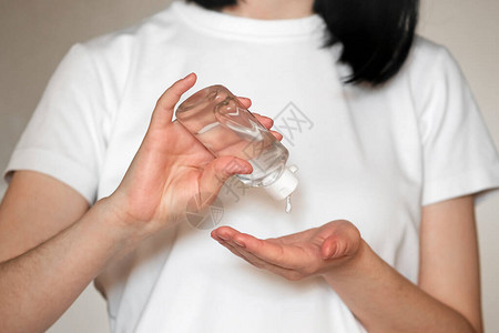 妇女在手上的瓶子中使用抗菌消毒剂凝胶的特写图片