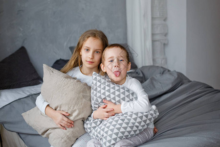 一个小男孩和一个穿睡衣的女孩在灰色卧室的床上枕头打斗他们喜欢这个游戏图片