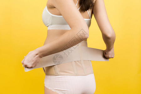 穿着支撑绷带的孕妇在黄色背景下穿上支撑绷带以减少背痛的后视图图片
