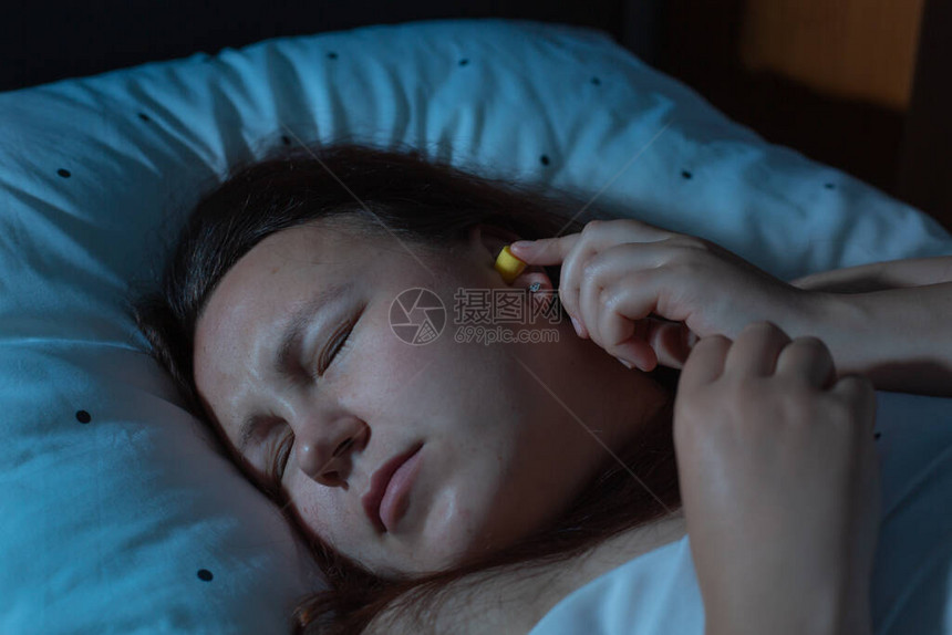 年轻妇女在睡前失眠前将耳塞入耳朵图片