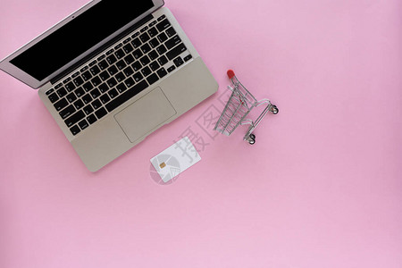 带空白信用卡的电脑笔记本电脑和粉红色背景的迷你购物车或手推车图片