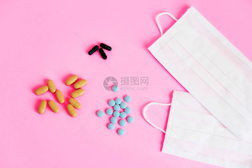 粉红色背景中的医用防护织物口罩和药物片剂图片