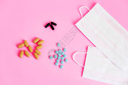 粉红色背景中的医用防护织物口罩和药物片剂图片