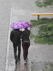 人们在一把粉红色的雨伞下穿着深色衣服图片