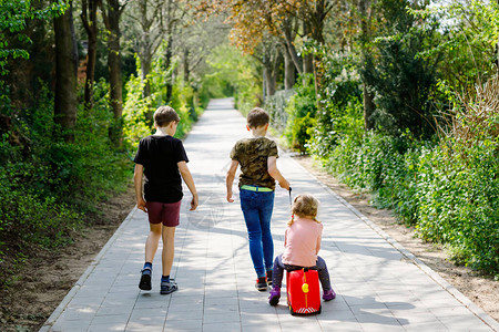 蹒跚学步的小女孩和两个男孩在公园流行的冠状中行走图片