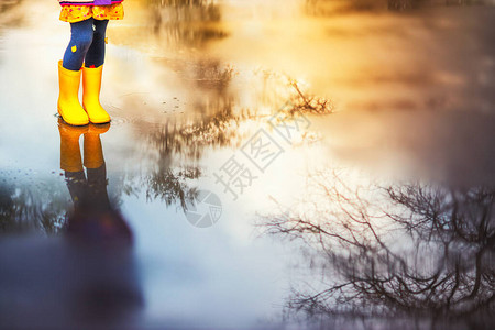 在春日散步时穿着黄色橡胶靴在水坑里跳图片