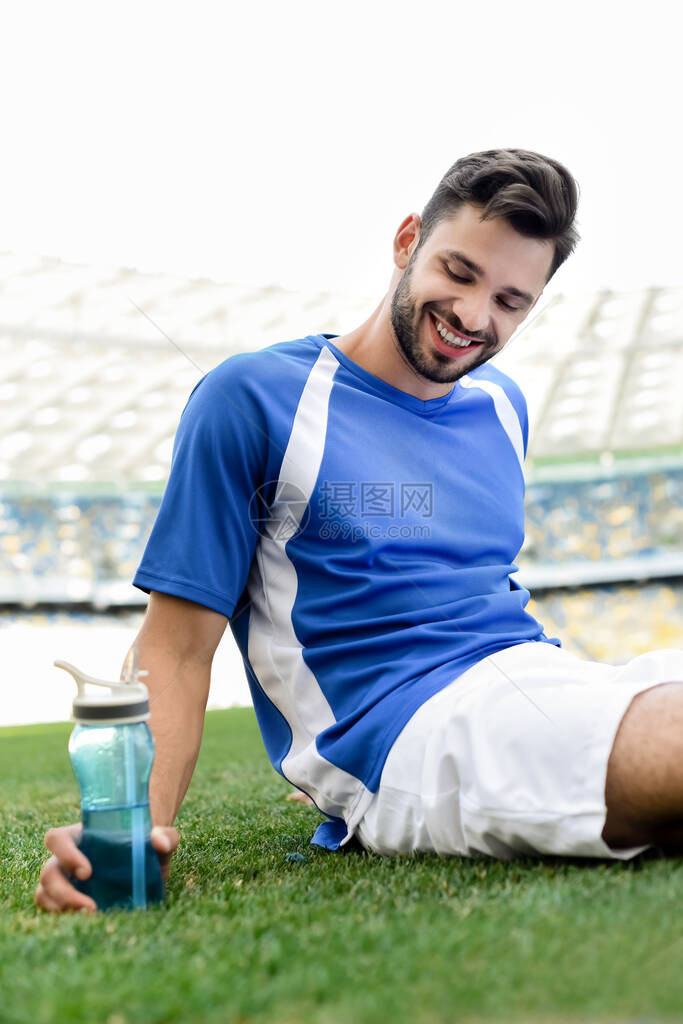 身着蓝白制服的职业足球运动员微笑着坐在足球场上图片