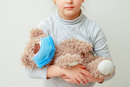 儿童在一个医疗面具中拿着玩具熊图片
