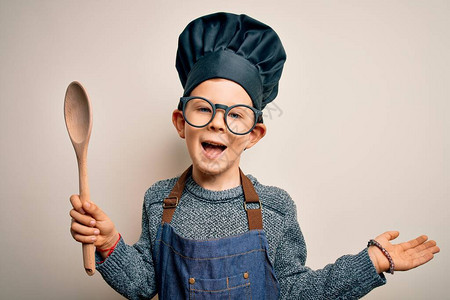 年轻的白人小厨师穿着厨师制服和帽子用木勺烹饪图片