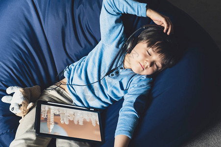 男孩躺在豆袋上听平板电脑上的音乐图片