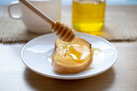 蜂蜜从烤面包机上的蜂蜜棒滴落背景杯与蜂蜜玻璃罐早餐和健图片