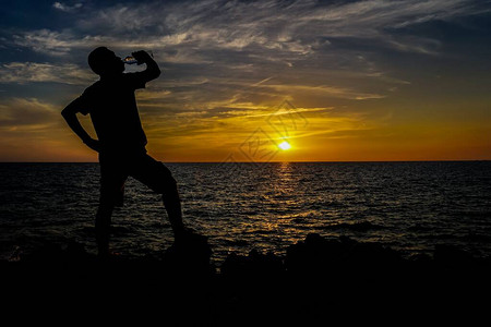 日落后站在海边喝水的人剪影图片